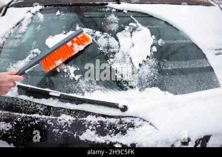 Problemi invernali con la vettura. Un uomo pulisce l'auto dalla neve con una spazzola Foto Stock