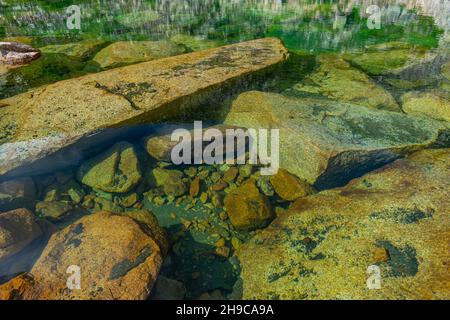 Grandi blocchi di granito e molte piccole pietre si trovano sotto l'acqua limpida e limpida sul fondo del lago Foto Stock