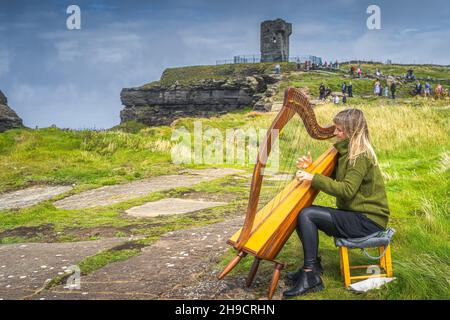 Doolin, Irlanda, agosto 2019 Donna che gioca arpa sulla cima delle scogliere iconiche di Moher, popolare attrazione turistica, Wild Atlantic Way, County Clare Foto Stock