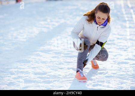 giovane donna infelice in giacca bianca con dolore alle gambe all'aperto nel parco della città in inverno. Foto Stock