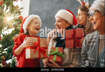 Buon Natale e buone feste. Bambini allegri che presentano i regali alla mamma e alla nonna. I genitori e i bambini piccoli che si divertono vicino all'albero al coperto. Amare Foto Stock