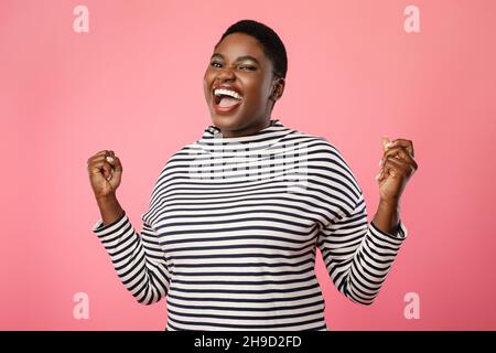 Joyful Plus-Size Black femmina che urla gesturando Sì su sfondo rosa Foto Stock