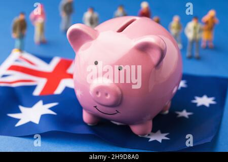 Piggy banca, bandiera australiana e giocattoli di plastica uomini su uno sfondo colorato, il concetto sul tema del reddito della popolazione australiana Foto Stock