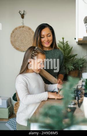 Mamma e la sua figlia di sei anni stanno facendo biscotti di Natale zenzero in cucina, stendendo l'impasto Foto Stock