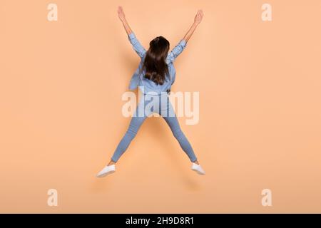 Foto full size di funky spensiered ragazza saltare alzare le mani in vittoria miglioramento personale isolato su sfondo di colore beige Foto Stock