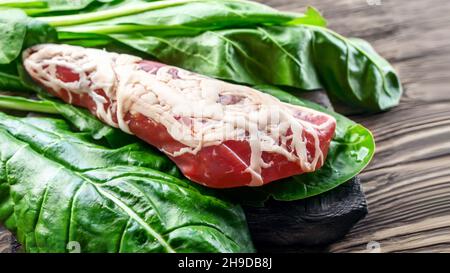 grande pezzo di carne secca in una sottile maglia di grasso interno. Un pezzo di carne fresca affumicata giace sulle foglie di spinaci. Filetto di carne di cervo naturale con erbe aromatiche Foto Stock