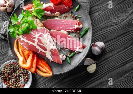 grande pezzo di carne secca in una sottile maglia di grasso interno. Un pezzo di carne fresca affumicata giace sulle foglie di spinaci. Filetto di carne di cervo naturale con tomat Foto Stock