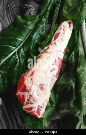 grande pezzo di carne secca in una sottile maglia di grasso interno. Un pezzo di carne fresca affumicata giace sulle foglie di spinaci. Filetto di carne di cervo naturale con erbe aromatiche Foto Stock