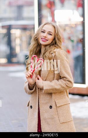 Una ragazza dolce da sogno, una giovane donna che tiene un lecca lecca in forma di cuore in una giornata invernale. Il concetto di Natale o San Valentino Foto Stock