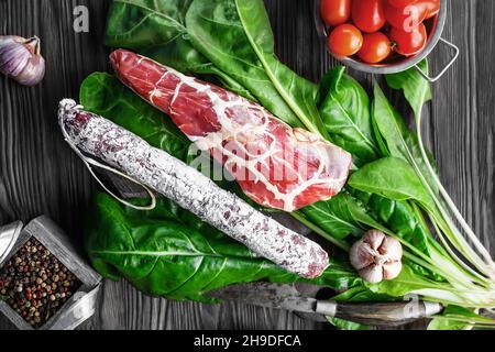 Salame salsiccia e carne secca in una sottile griglia di grasso sulle foglie di spinaci. Salsiccia italiana tagliata in verdure Foto Stock