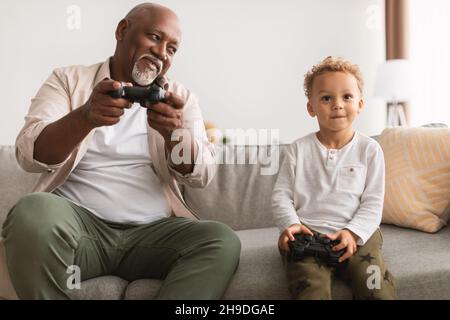 Black Grandfather e Grandson che giocano con videogiochi che si divertano a casa Foto Stock