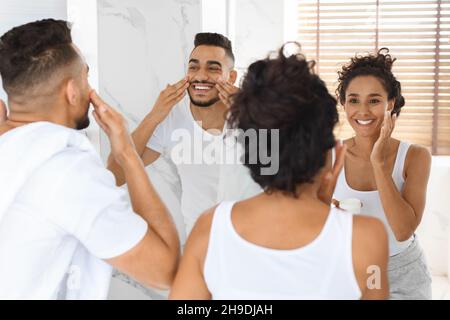 Coppia felice Medio Oriente applicazione crema viso vicino specchio in bagno Foto Stock