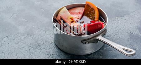 VIN brulé bevanda calda con agrumi, mela, melograno e spezie in casseruola di alluminio con giocattoli d'epoca albero di Natale e ramo di Fir su bac calcestruzzo Foto Stock