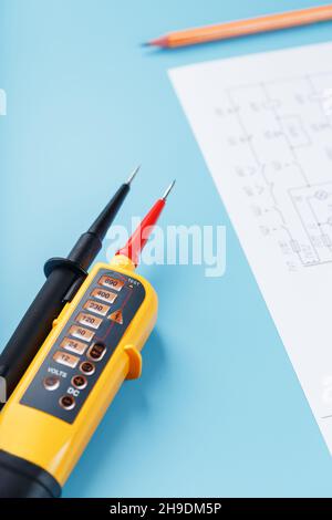 Indicatore di tensione giallo con uno schema elettrico su sfondo blu. Test e verifica delle reti elettriche Foto Stock