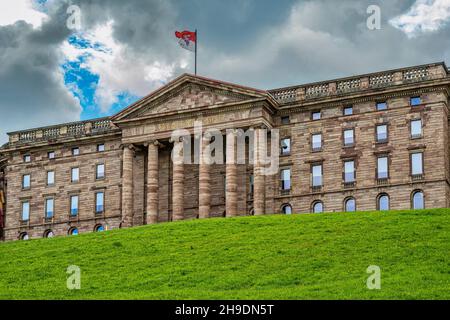 Castello di Wilhelmshoehe immerso nel verde del suo parco, la bandiera tedesca sbatte sul palo della bandiera. Kassel, Bergpark Wilhelmshöhe, Germania Foto Stock