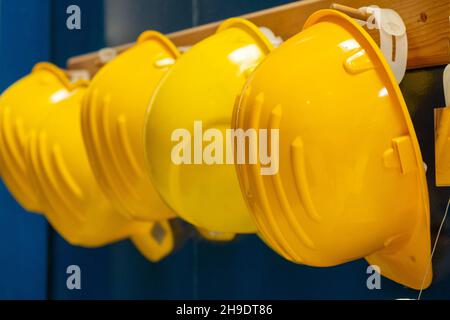 Linea di nuovi caschi protettivi gialli per lavoratori appende su barra di legno in spogliatoio di produzione di impianti vista estrema ravvicinata Foto Stock