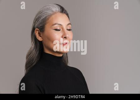 Donna bianca asiatica matura in posa con i suoi occhi chiusi isolato su sfondo grigio Foto Stock