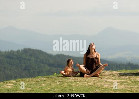 Madre in posa di loto in montagna con figlia piccola. Foto Stock
