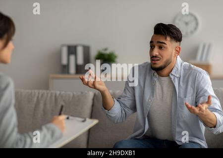 Uomo arabo sottolineato ed emotivo che soffre di depressione, consigliere che fornisce assistenza professionale presso l'ufficio medico Foto Stock