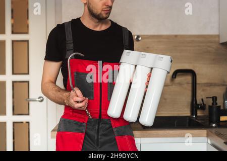 Idraulico in cucina che tiene la casa a tre stadi fiasca sistema di purificazione dell'acqua Foto Stock