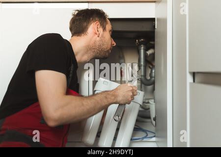 Idraulico in cucina installa un sistema di trattamento delle acque domestiche. Sistema per fiasche a tre stadi Foto Stock