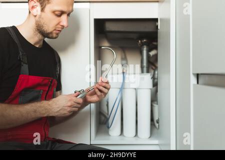 Idraulico in cucina installa il rubinetto per il sistema di depurazione delle acque domestiche. Sistema per fiasche a tre stadi Foto Stock