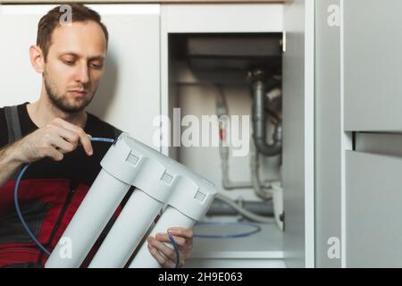 Idraulico in cucina installa un sistema di trattamento delle acque domestiche. Sistema per fiasche a tre stadi Foto Stock