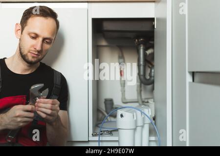 Idraulico in cucina installa un sistema di trattamento delle acque domestiche. Sistema per fiasche a tre stadi Foto Stock