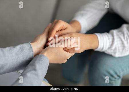 Supporto psicologico. Psicoterapeuta che offre aiuto alla giovane donna, tenendo le mani durante la sessione di psicoterapia Foto Stock