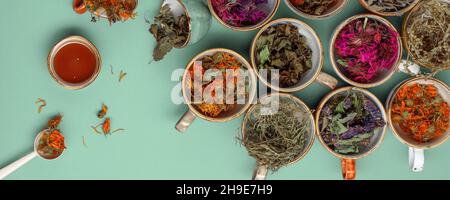 Assortimento di erbe di tè secche e rilassanti in tazzine colorate su sfondo verde menta con miele. Calendula, menta, issopo di anice, mondarda didima, legno di wormwood, Foto Stock