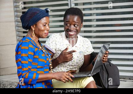 belle donne d'affari che si siedono all'aperto lavorando con un computer portatile mentre ridono. Foto Stock