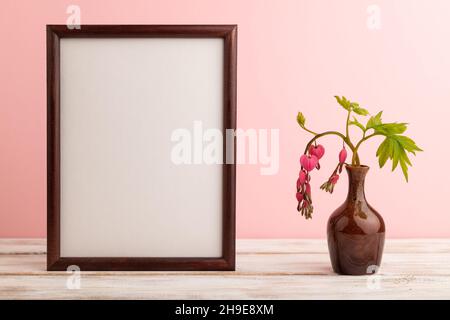 Cornice in legno con dicentra rosa, cuore rotto in vaso in ceramica su sfondo rosa pastello. Vista laterale, copia spazio, mockup, dima, primavera, estate minim Foto Stock