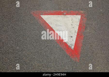Questo cartello stradale, che è stato dipinto sulla superficie asfaltata della strada e dice: Dare via. Foto Stock