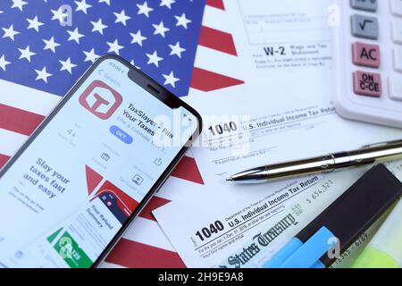 KHARKOV, UCRAINA - 5 MARZO 2021: Applicazione TaxSlayer su iPhone 12 schermo pro con 1040 e w-2 carta fiscale forma sulla bandiera degli Stati Uniti Foto Stock