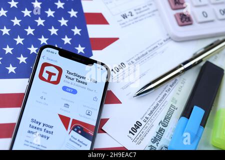 KHARKOV, UCRAINA - 5 MARZO 2021: Applicazione TaxSlayer su iPhone 12 schermo pro con 1040 e w-2 carta fiscale forma sulla bandiera degli Stati Uniti Foto Stock