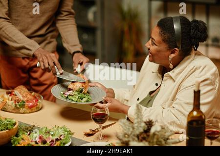 Primo piano dell'irriconoscibile uomo afro-americano che serve pollo mentre si gusta la cena con la famiglia Foto Stock