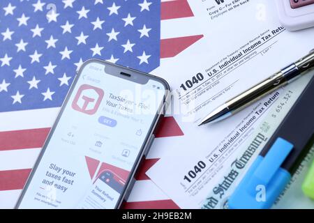 KHARKOV, UCRAINA - 5 MARZO 2021: Applicazione TaxSlayer su iPhone 12 schermo pro con 1040 e w-2 carta fiscale forma sulla bandiera degli Stati Uniti Foto Stock