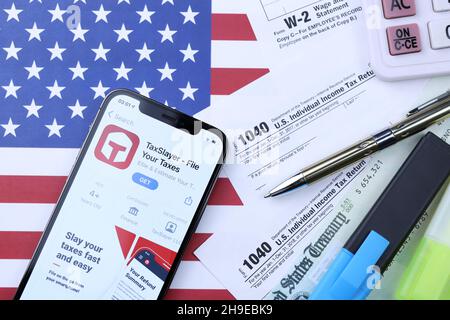 KHARKOV, UCRAINA - 5 MARZO 2021: Applicazione TaxSlayer su iPhone 12 schermo pro con 1040 e w-2 carta fiscale forma sulla bandiera degli Stati Uniti Foto Stock