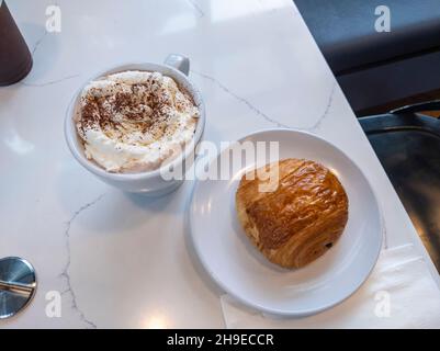Vista dall'alto di un caffè con panna montata e pain au chocolat su un tavolo bianco in marmo. Foto Stock