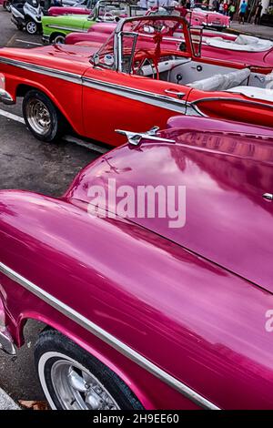 Una linea di auto classiche americane dipinte in colori brillanti che sono disponibili a noleggio nella città vecchia di Havana. Foto Stock