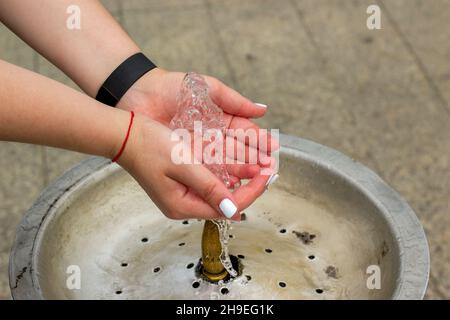 Le donne giocano a mano con spruzzi d'acqua pulita e fresca, in una fontana. Belle donne mani in uno spruzzo d'acqua da una fontana della città. Mani donne wa Foto Stock