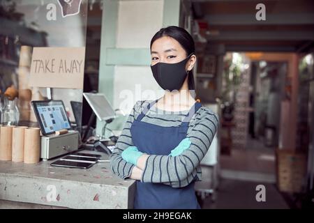 Ritratto di giovane donna in maschera di viso che lavora in caffè Foto Stock