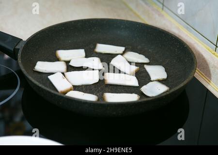 Il processo di cottura delle uova strapazzate con lo strutto e la salsiccia. L'uomo prepara due porzioni. Pezzi di pancetta sono fritti in una padella. Foto Stock