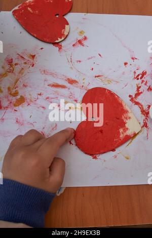 Sessione di San Valentino e d'arte. Le mani del bambino dipingono il cuore rosso Foto Stock