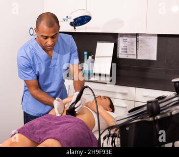 Cosmetologo che esegue la cavitazione ecografica del corpo procedura per il cliente femminile Foto Stock