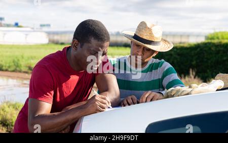 I giardinieri firmano i documenti vicino l'automobile sul campo di fattoria Foto Stock