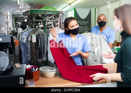 Operai di lavanderia in maschere protettive che danno vestiti al cliente Foto Stock