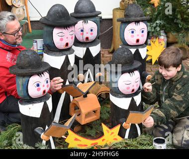 05 dicembre 2021, Sassonia, Borsdorf: Denny Pfaff (l) e suo figlio Felix stanno riparando la vernice scheggiata sui cantanti di carol che decorano il giardino anteriore delle famiglie di Pfaff. I cantanti, alti fino a 1.20 metri, sono stati realizzati dal forestiero Manfred Pfaff oltre 10 anni fa con una motosega di pino Weimut. Essi deliziano la gente della comunità sassone di Wermsdorf e passando automobilisti ogni anno fino al 6 gennaio. I carolers in legno appartengono a circa 50 figure segate a mano, funghi, panchine di fiori e disposizione dei posti a sedere che l'artista di motosega hobby ha fatto. Foto: Waltraud Grubitzsch/dpa-Zen Foto Stock