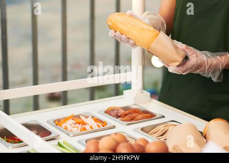 Immagine ritagliata del fornitore in guanti protettivi che mettono il sandwich in una confezione di cartone Foto Stock