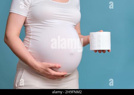 Carta igienica nelle mani di una donna incinta, studio girato su uno sfondo blu Foto Stock